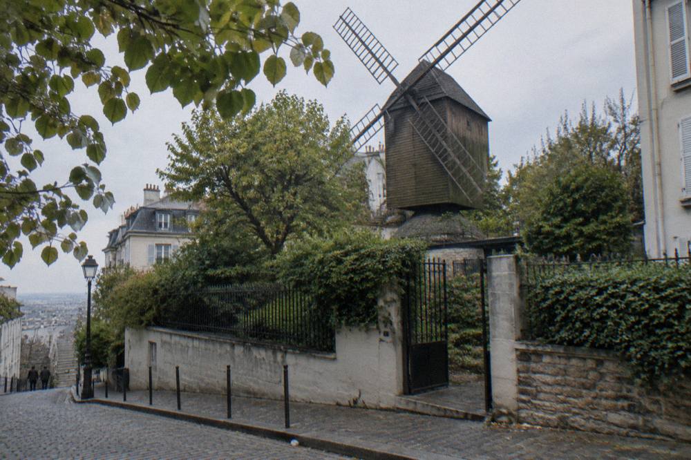 A historic Paris windmill building beside a sloping tree-lined street