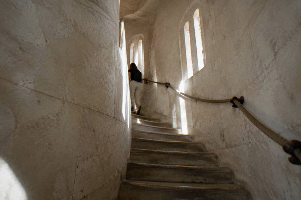 A narrow stone spiral staircase inside the Sacre-Coeur dome lit by small windows