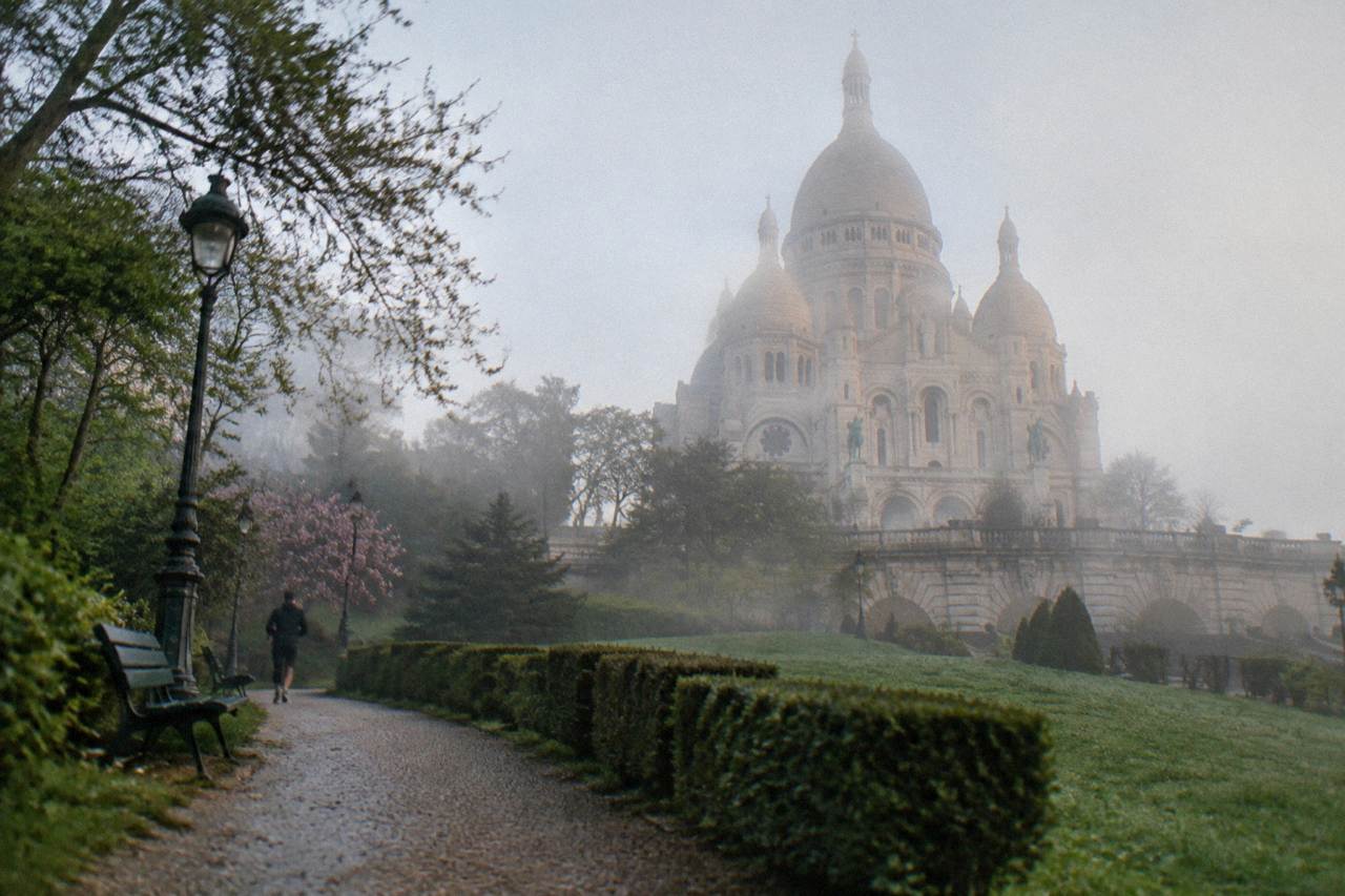 The white stone exterior and domes of the Sacre-Coeur basilica seen from the gardens below