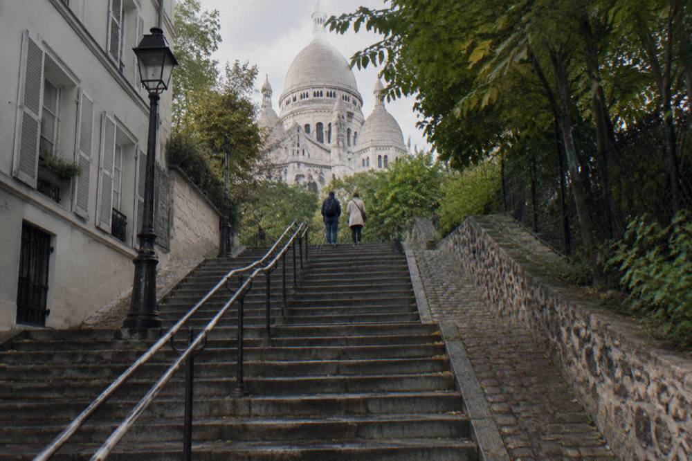 Stone steps of a cobbled Montmartre street rising between old buildings toward the basilica