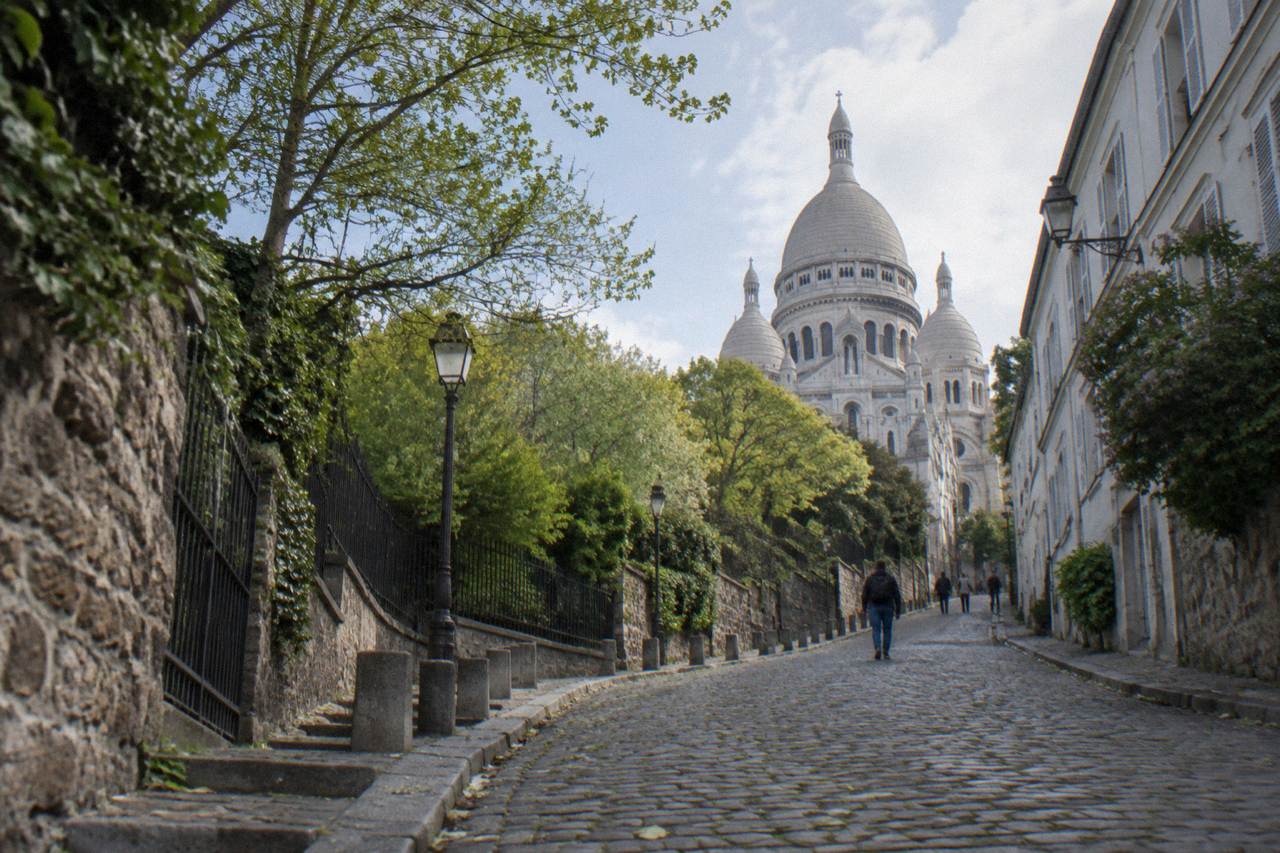 Cobbled street rising toward the white domes of the Sacre-Coeur basilica on the hill above