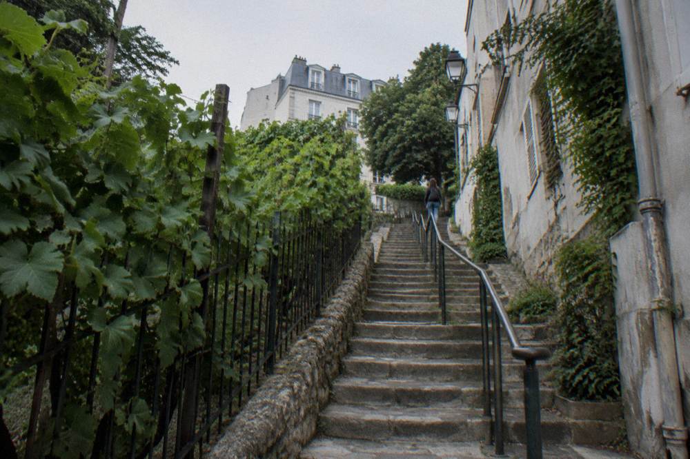 A narrow sloping lane in Montmartre with stone steps between old buildings leading up the hill