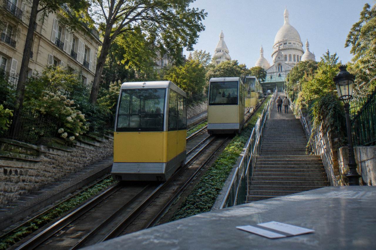The Montmartre funicular cabins beside the stairway leading up toward the Sacre-Coeur basilica on a bright day