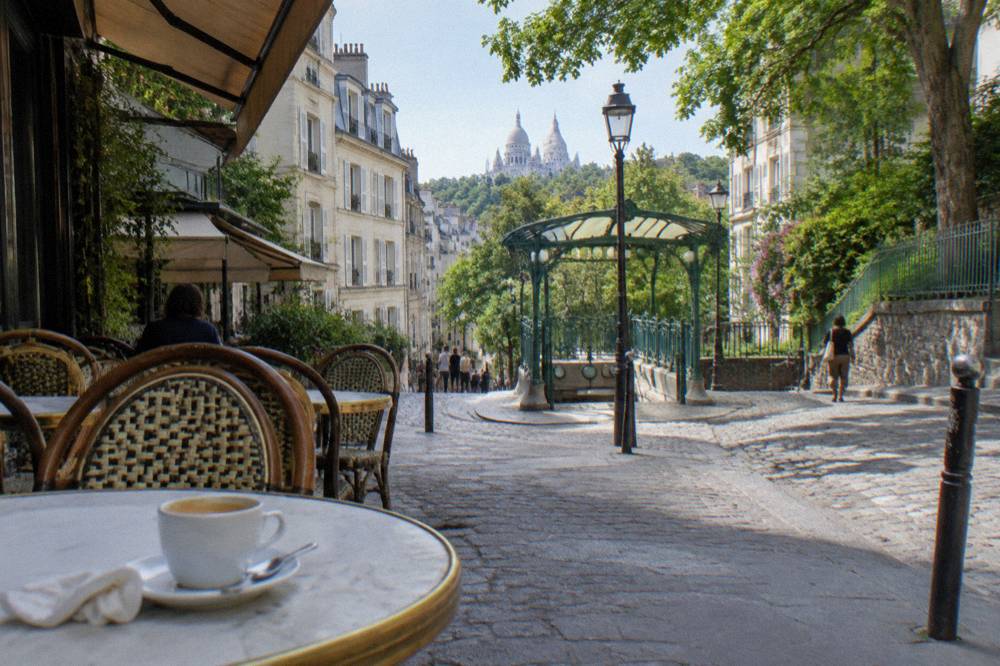 Cafe tables and awnings along a sloping Montmartre food street in morning light