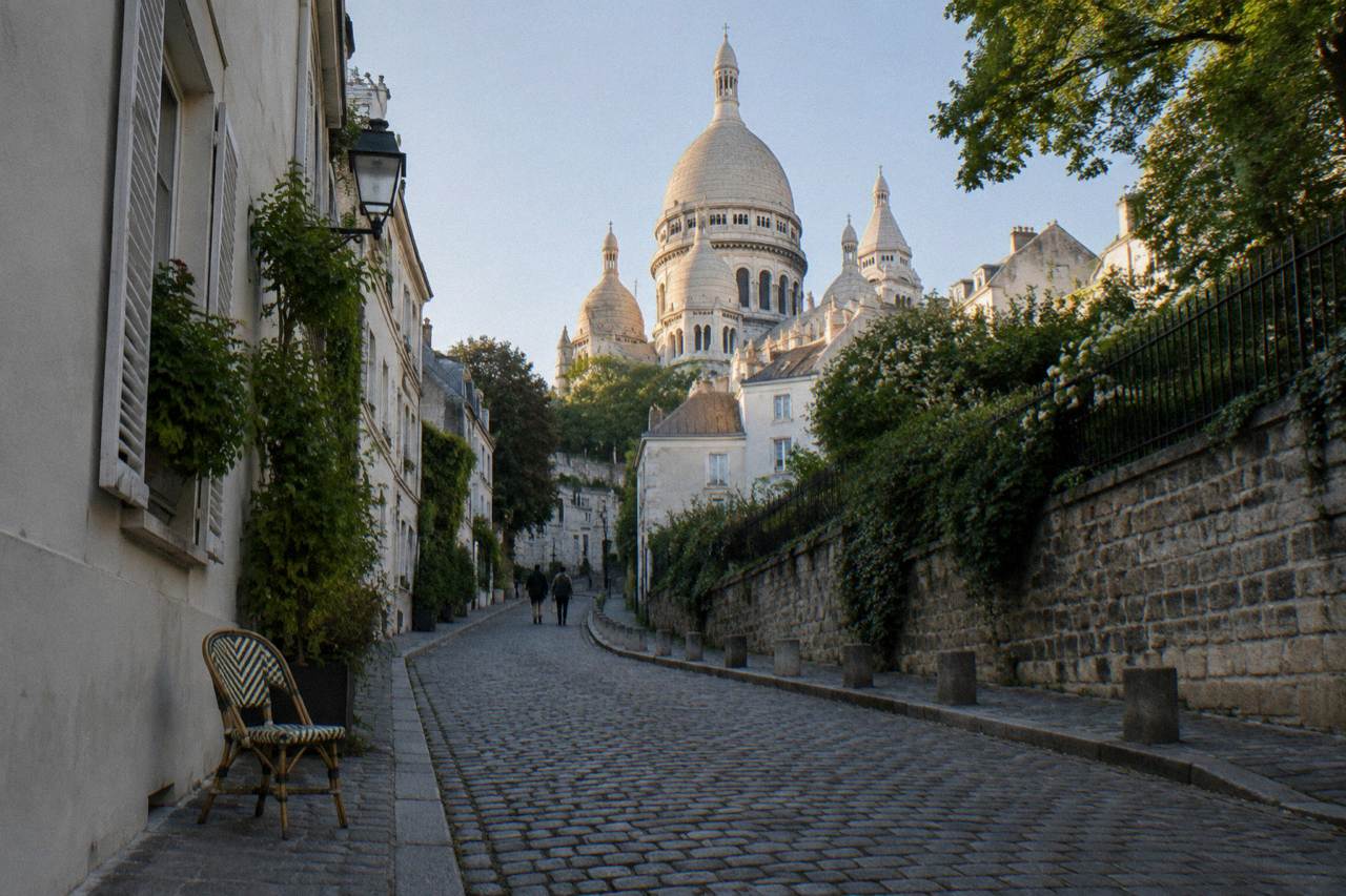 Cobbled Montmartre street rising toward the white domes of Sacre-Coeur basilica under a clear sky