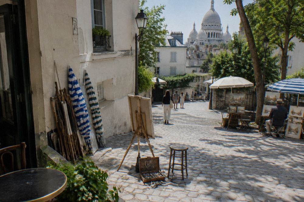 Artists' easels and umbrellas on the open square of Place du Tertre with the basilica behind the rooftops