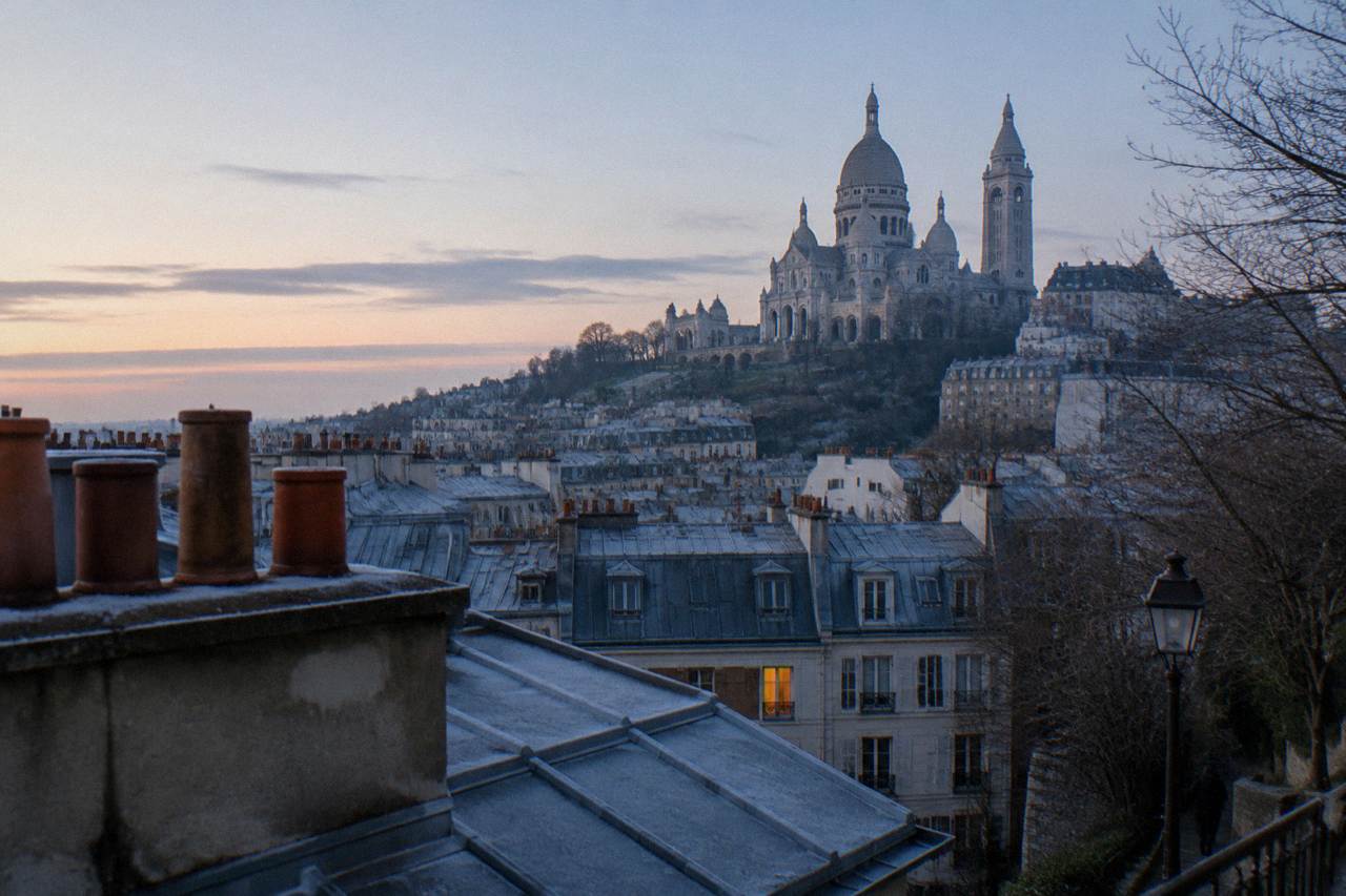 View across Paris rooftops from the hill of Montmartre toward the white domed basilica at the top