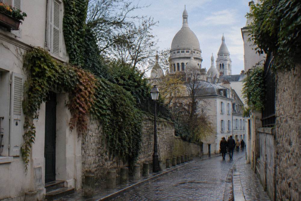 The basilica's white domes seen from a narrow Montmartre street of low stone buildings