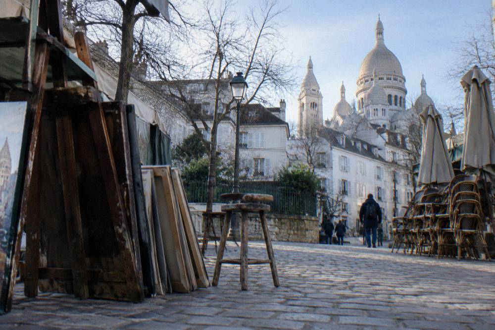 Artists' easels and cafe tables on a small square in front of a church in Montmartre