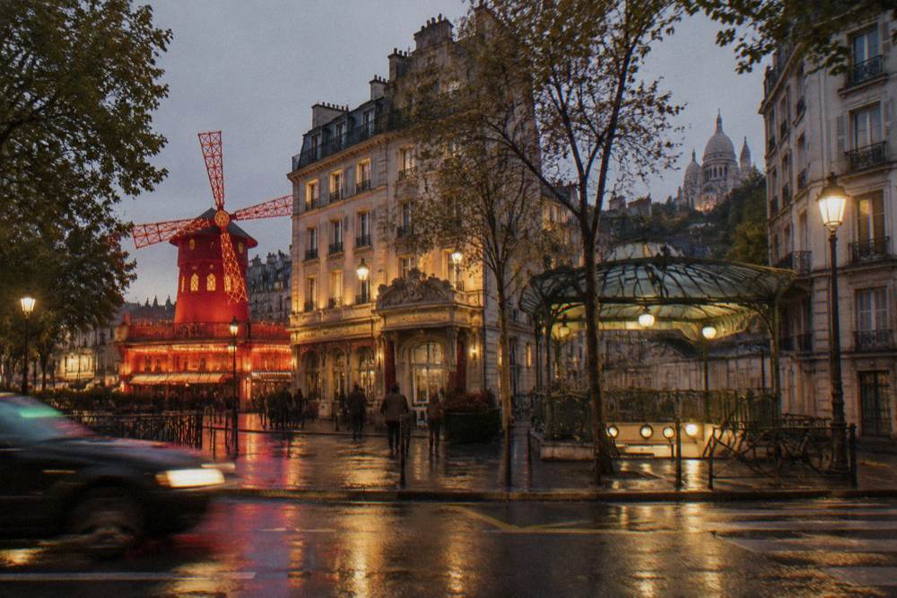 A wide Paris boulevard at dusk with lit theatre facades and a metro entrance