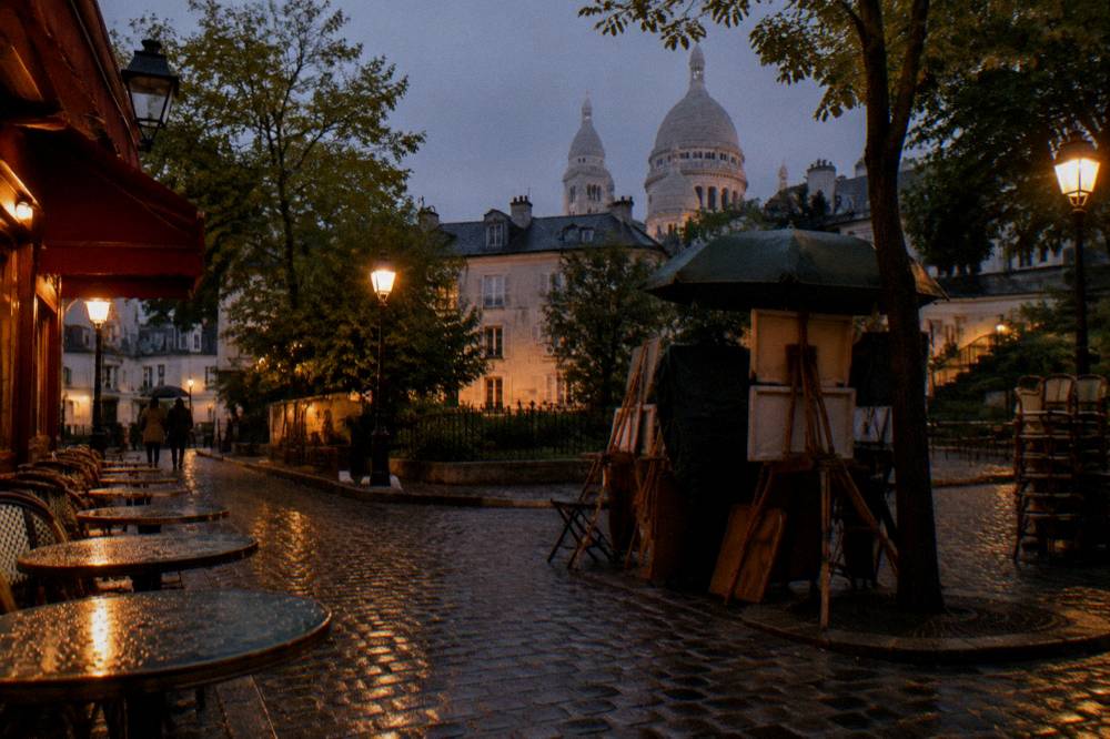 A lit restaurant terrace on a Montmartre corner street at night with empty tables