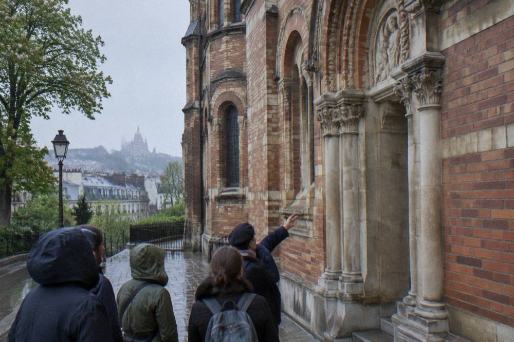 Guide pointing out carvings on a Montmartre building facade to visitors