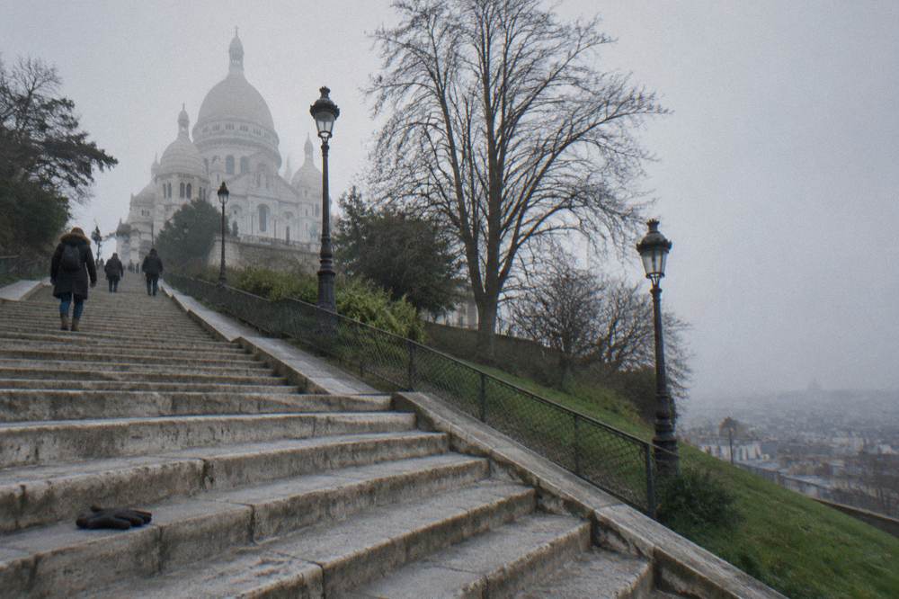Wide stone staircase ascending toward the white basilica with the city skyline behind