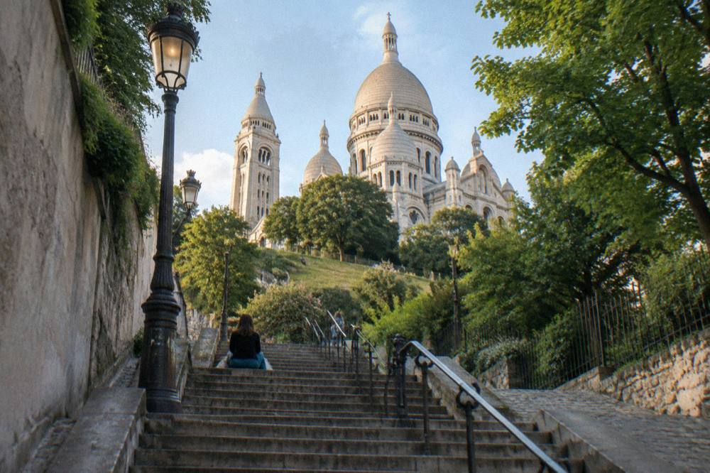 A stone stairway climbing between Paris buildings toward a white domed church above