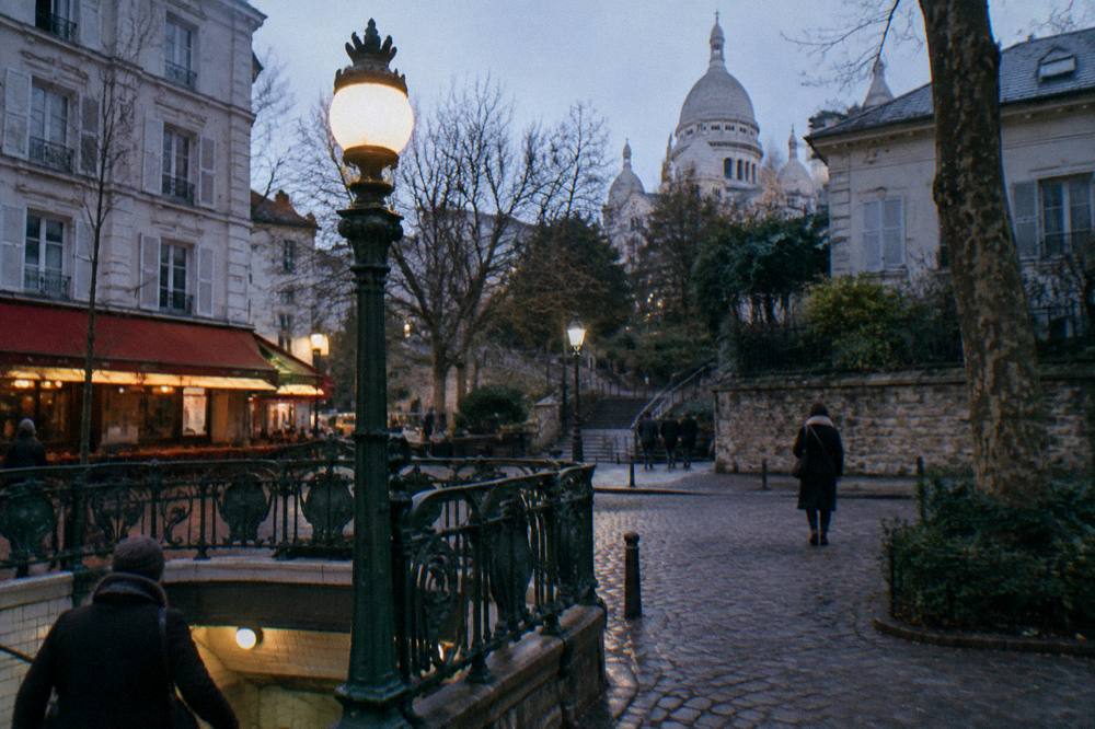 A Paris metro entrance with an ornate green iron frame and lamp on an evening street