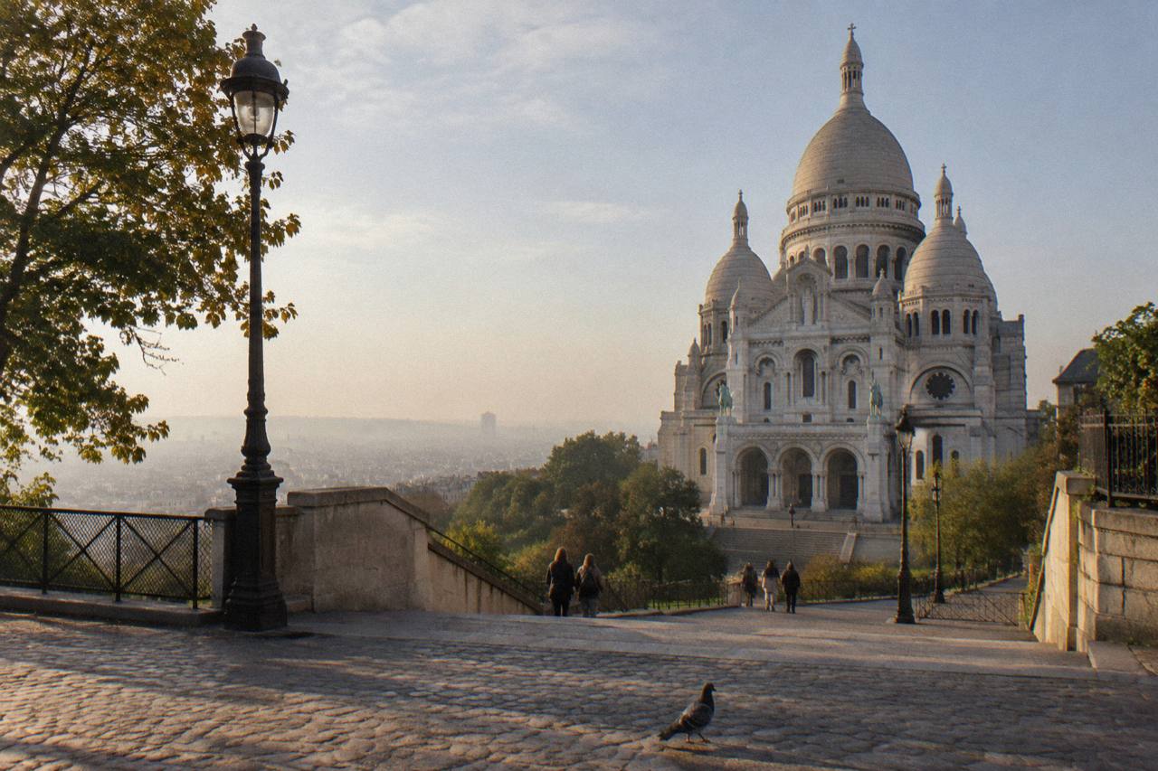 Montmartre hillside seen from below, with the white domes of Sacre-Coeur Basilica rising above Paris rooftops in warm evening light, an area explored on guided Montmartre walking tours.